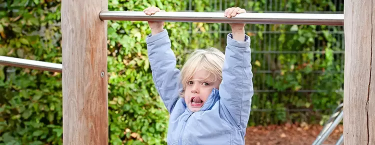 Blond meisje in licht blauwe jas hangt aan een rekstok op het schoolplein
