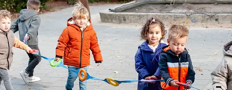 kinderen van een jaar of 4 houden een touw vast om samen veilig te wandelen