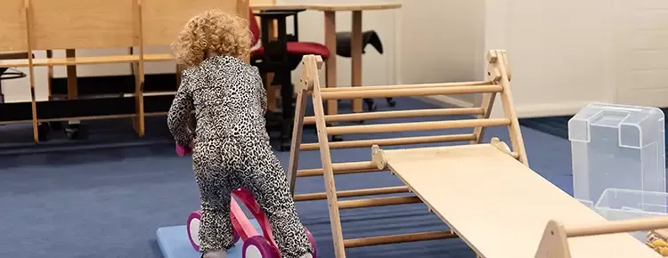 Meisje met krullen stapt op een loopfiets in de gymzaal