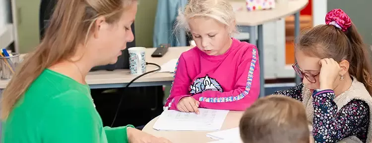 docent helpt 3 kinderen met hun schoolwerk