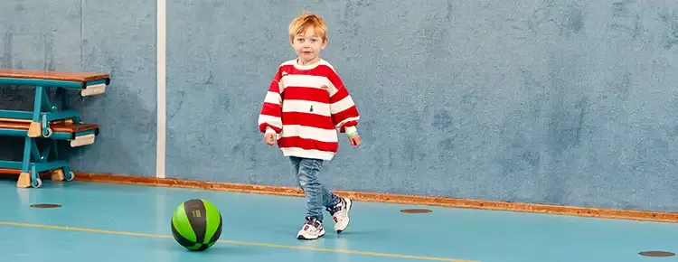 Jongen van een jaar of 4 loopt in de gymzaal naar een bal om deze te trappen