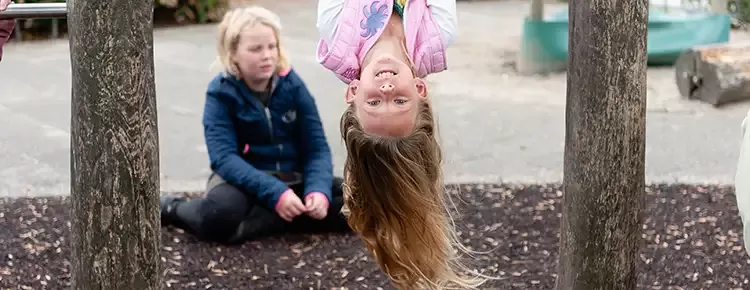 Meisje in roze jas hangt ondersteboven aan een rekstok